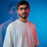 Half-length portrait of a person in an oversized white t-shirt, featuring a dreamlike editorial style with multi-exposure motion blur, vertical streaks, and a deep azure to cyan gradient background. Dramatic lighting uses a cool blue wash with orange/yellow edge glow.