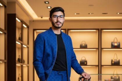 4K ultra-realistic DSLR photo of a handsome Asian man in a royal blue Gucci monogram jacket and pants, black T-shirt, and sneakers, standing next to a luggage cart with a black Gucci backpack and a trolley in a high-end luxury boutique with designer bags displayed.