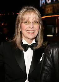 Diane Keaton smiling in her signature wide-brimmed hat and tailored suit, representing her timeless Hollywood style.