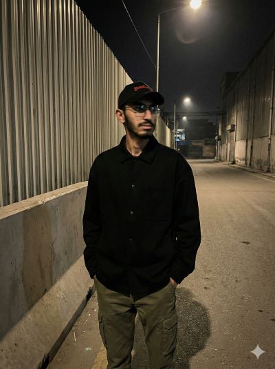 Young man in black jacket and olive cargo pants standing in industrial alley at night with street lights